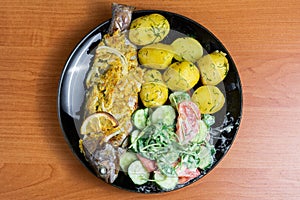 Baked trout with lemon on a plate with arugula, tomato, cucumber salad and young potatoes with dill