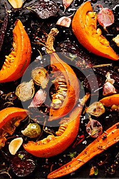 Baked vegetables with the addition of olive oil, aromatic herbs and spices on a dark background