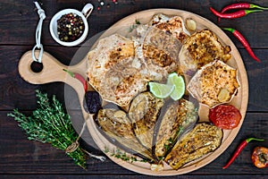 Baked vegetables: eggplant, patisson, tomatoes on a round wooden stand on a dark background.