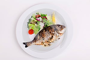 Baked whole fish grilled on a plate with vegetables and lemon