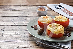 Baked whole tomatoes stuffed with mushrooms and cheese with seasonings on a wooden background. Copy space