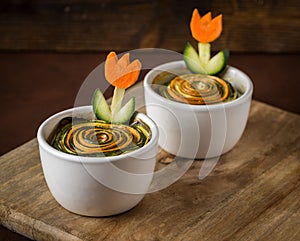 Baked zucchini with carrot in white bowl on wooden background.