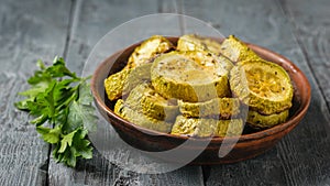 Baked zucchini slices in a clay bowl on a black wooden table. Vegetarian dish. Natural plant food