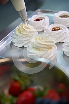 Baker adding custard from pastry bag at top of merengue nest photo