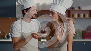 Baker and assistant putting cherry on cake at kitchen. Couple of confectioners