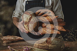 Baker in black apron holds variety of bread