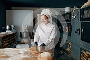 Baker chef holding knife and cutting fresh bread on wooden table