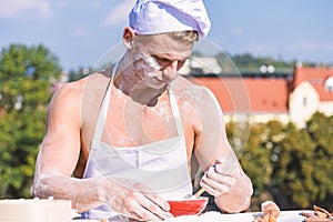Baker concept. Cook or chef with sexy muscular shoulders and chest covered with flour. Man on busy face wears cooking