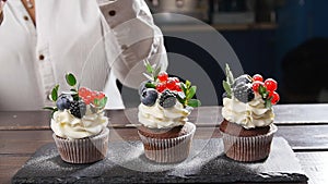 Baker decorating tasty cupcake. Icing sugar sprinkled on cake