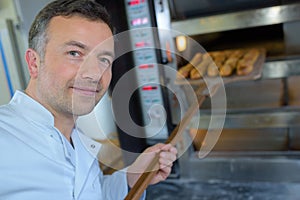 Baker getting fresh bread out traditional oven