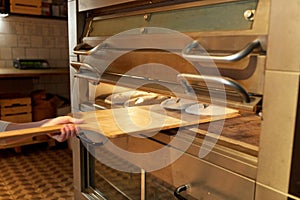 Baker hand putting dough into bread oven at bakery