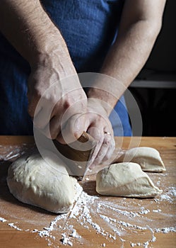 Baker hands cutting off piece of dough with old dough scrapper over bakery table surface