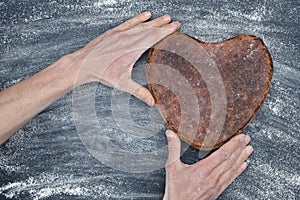 Baker hands gently holds rye whole grain yeast-free sourdough bread in shape of heart on black table with white flour