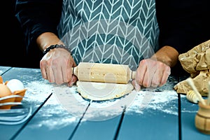 Baker hands preparing fresh dough with rolling pin on kitchen table