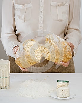 Baker holds in his hands a freshly baked sourdough bread, broken in half