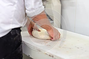 Baker kneading fresh raw bread dough at the bakery.