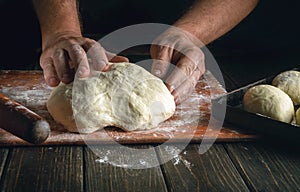 The baker kneads the dough on the kitchen board with flour powder for pies. The concept of baking and pastry in the bakery