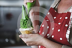Baker piping icing onto a cupcake