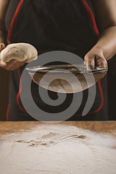 Baker pours flour for making pizza. Chef cooking dough to bake a cake on a wooden table.