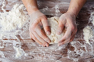 Baker prepares the dough on a wooden table, male hands knead the dough with flour