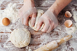 Baker prepares the dough on a wooden table, male hands knead the dough with flour