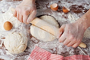 Baker prepares the dough on a wooden table, male hands knead the dough with flour