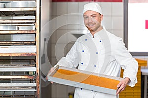 Baker presenting a tray of fresh dough in bakery