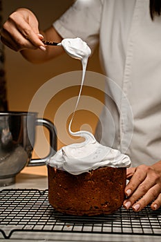 Baker puts with spoon white cream on the Easter cake