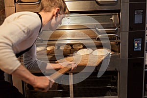 Baker putting dough into bread oven at bakery