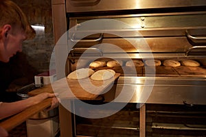 Baker putting dough into bread oven at bakery