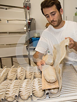 Baker putting unbaked bread dough into hot oven in bakery