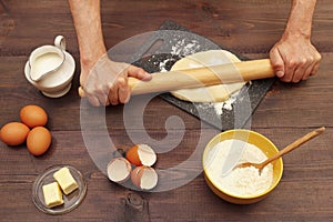 Baker rolling dough with rolling pin on the board on rustic table