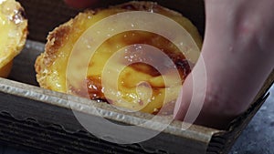 A baker's or cook's hand places a fresh and hot crispy puff pastry pie with egg custard into a paper package in