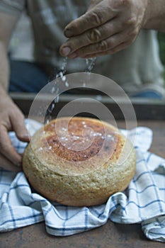 Baker& x27;s hand sprinkles flour on fresh bread close-up. A man finishes baking, decorates warm bread. Traditional