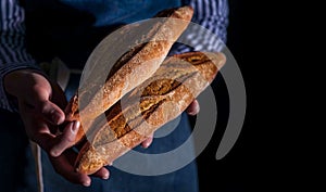 Baker`s hands hold fresh bread over dark background