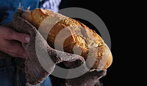 Baker`s hands hold fresh bread over dark background