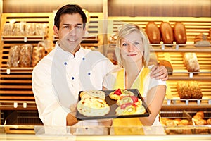 Baker and shopkeeper in bakery with tablet of cake