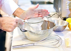 Baker sieving flour into a bowl in the kitchen of the bakery