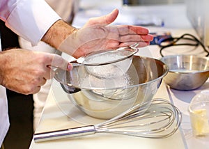 Baker sieving flour into a bowl in the kitchen of the bakery