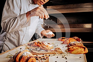 Baker standing near oven and decorating pastry desserts