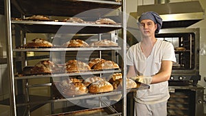 Baker taking a loaf of freshly baked bread from the oven in a modern bakery