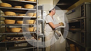 Baker taking a loaf of freshly baked bread from the oven in a modern bakery