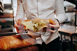 Baker in uniform breaks freshly baked bread at the bakery