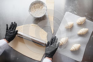 Baker rolling dough and preparing croissants in bakery