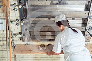 Baker woman getting bread loafs out of bakery oven