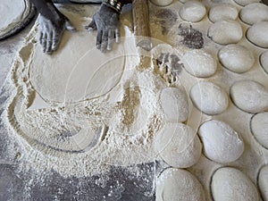 Baker working with flour and dough to make a pizza base.
