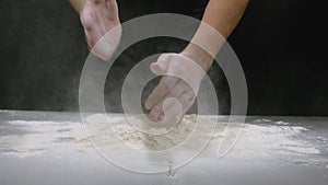 Bakers hands clap their hands filled with flour on a black background. The baker works with dough and flour. Baking
