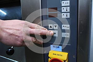 Baker hand pushing a power button on a control panel of an electric oven