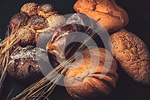 Bakery bread on a wooden table. Various bread and sheaf of wheat ears. Photo in the dark key