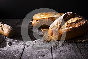 Bakery - gold rustic crusty loaves of bread and buns on black background.